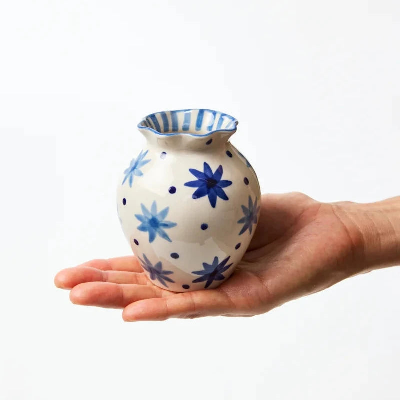 Hand holding a small ceramic vase with blue floral patterns on a white background