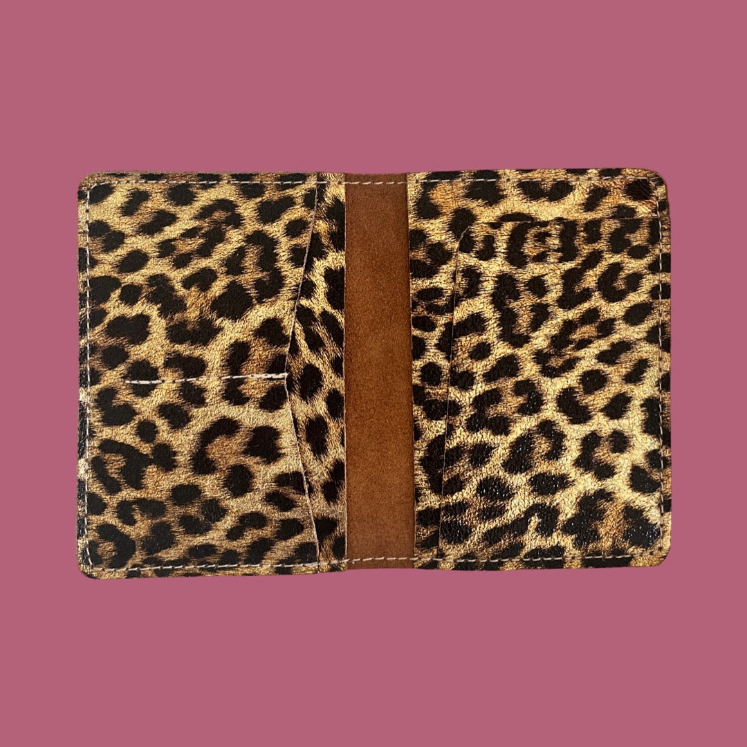 A leopard print leather passport holder shown open against a solid pink background.