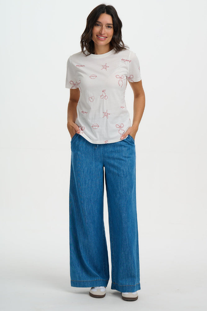 Woman wearing a white t-shirt with red patterns and blue pants on a white background