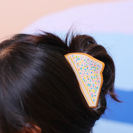 A hair claw in the shape of fairy bread in dark straight hair.