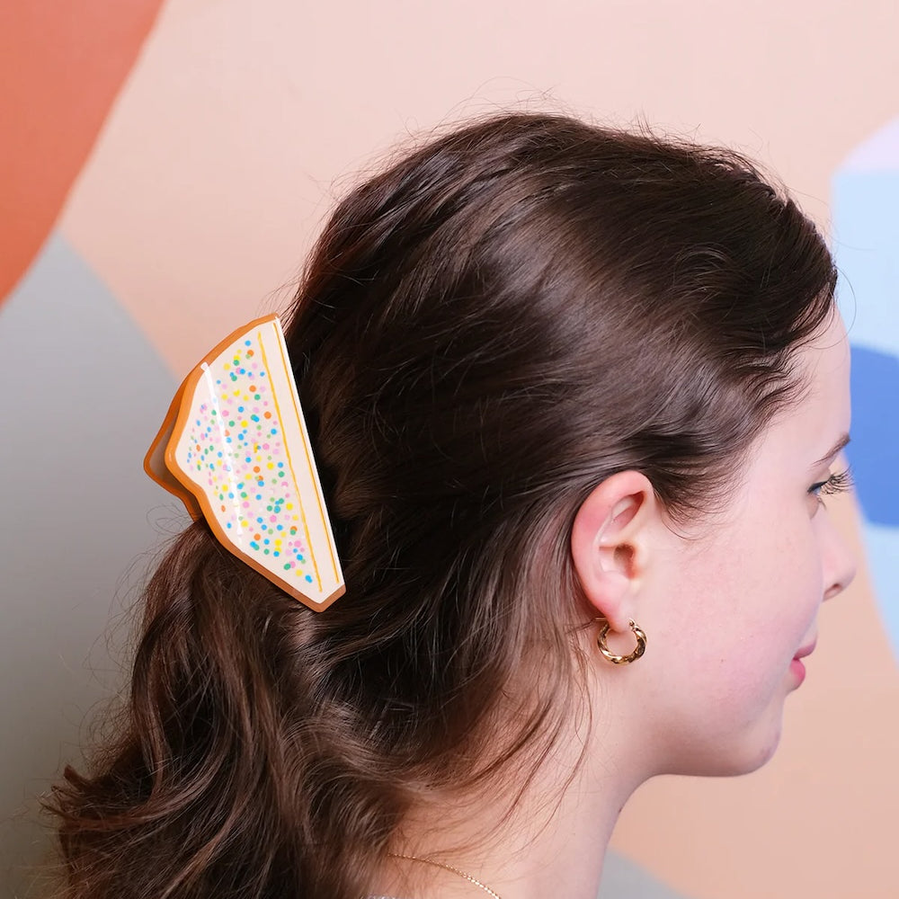 A hair claw in the shape of fairy bread in dark brown wavy hair.