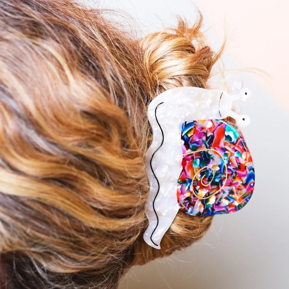 A colourful hair claw in the shape of a smiling snail in light wavy hair.