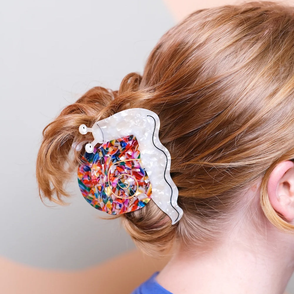 A colourful hair claw in the shape of a smiling snail in straight blond hair.