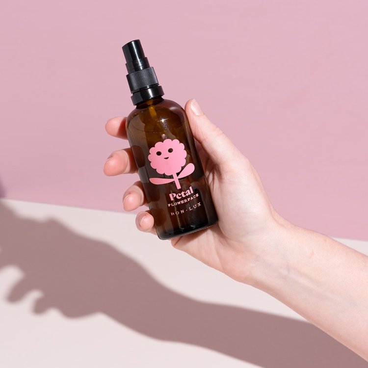 Hand holding a bottle of Bon Lux Flowerface Face Mist in Petal against a pink background.