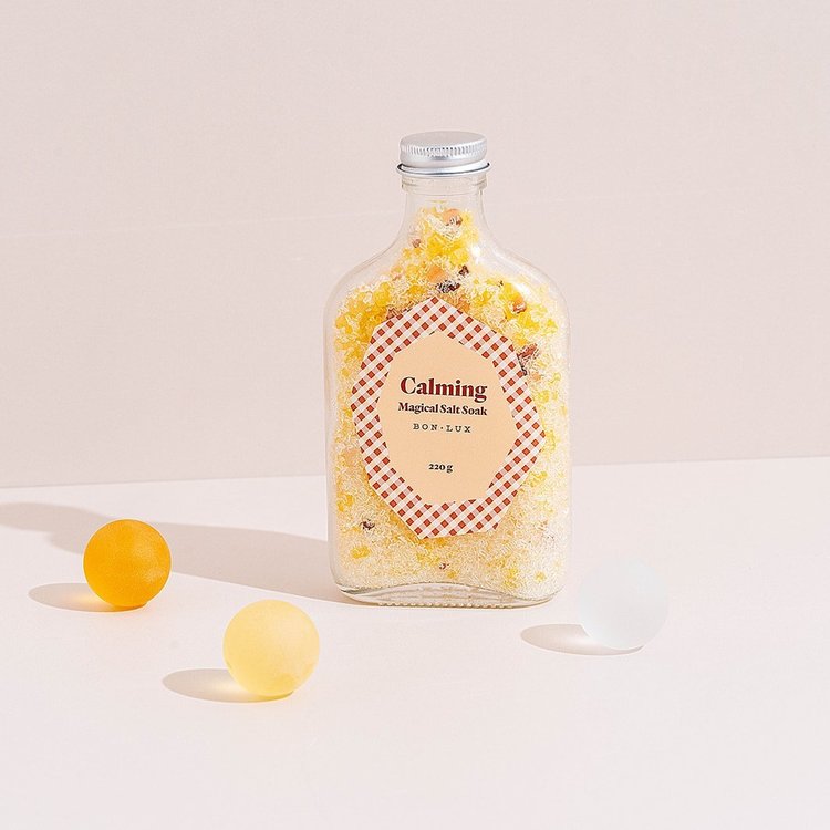 A bottle of Bon Lux Calming Magical Salt Soak with two yellow balls and a white ball on a light background.