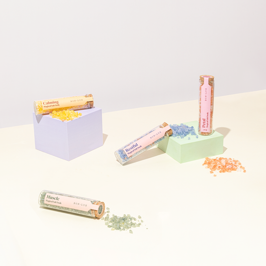 Tubes of Bon Lux Magical Salt Soak on a light surface with sprinkles of each salt