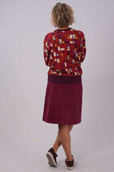 Full length back view of model wearing Essaye Abstract Sweater in Red, with red skirt and dark red coloured sneakers