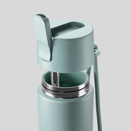 A close-up of a Fressko Ceramic Interior MOVE Drink Bottle - 660ml in Breezy, matte aqua blue-green insulated travel bottle with a flip-top lid and a carrying strap, and featuring a metal drinking straw connected to the flip-top lid and a matching colour ceramic interior, shown against a solid gray background.