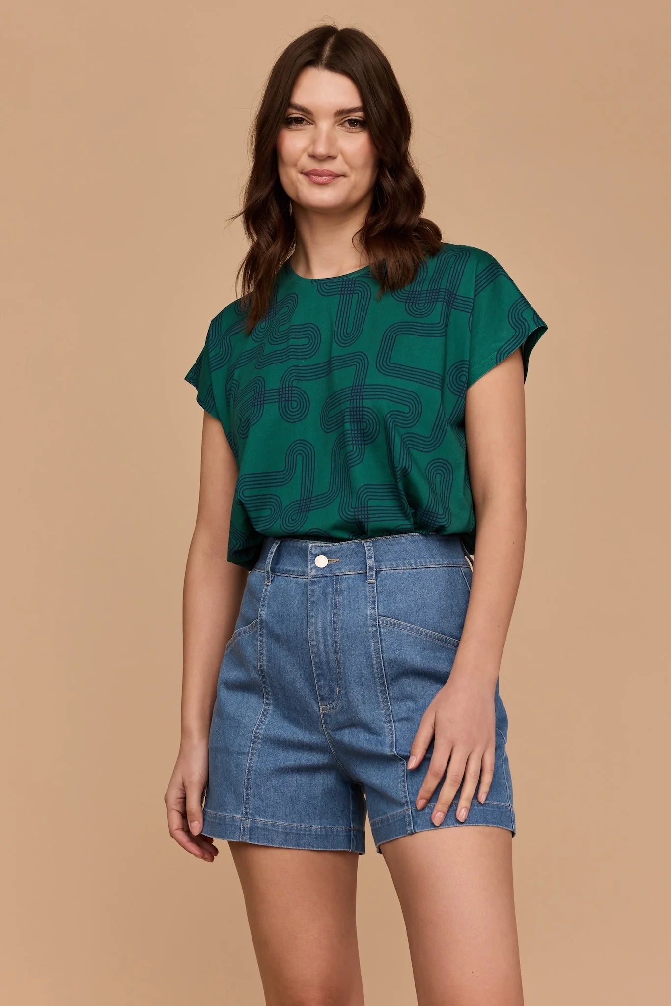 Model wearing Frock Me Out Labyrinth Capped Sleeve Tee (a green coloured top) and a pair of denim shorts