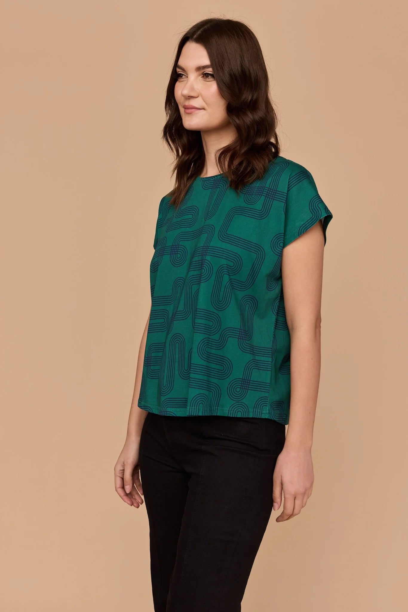Side view of a model wearing Frock Me Out Labyrinth Capped Sleeve Tee (a green coloured top) and a pair of black pants