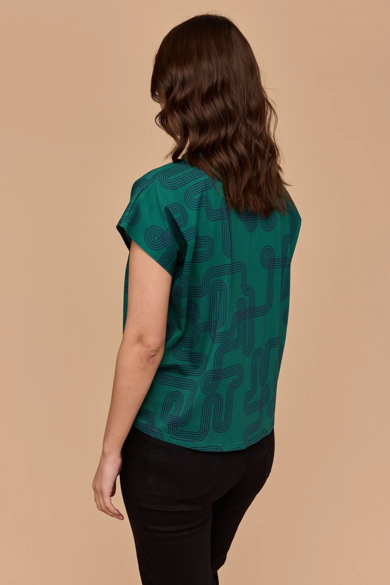 Back view of Model wearing Frock Me Out Labyrinth Capped Sleeve Tee (a green coloured top) and a pair of black pants