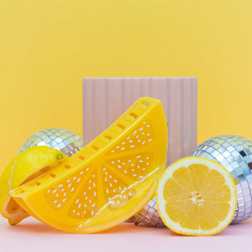 Styled image of Jenny Lemons XL Lemon Slice Hair Claw accompanied by lemon slices, mini disco mirror balls against a yellow coloured background.