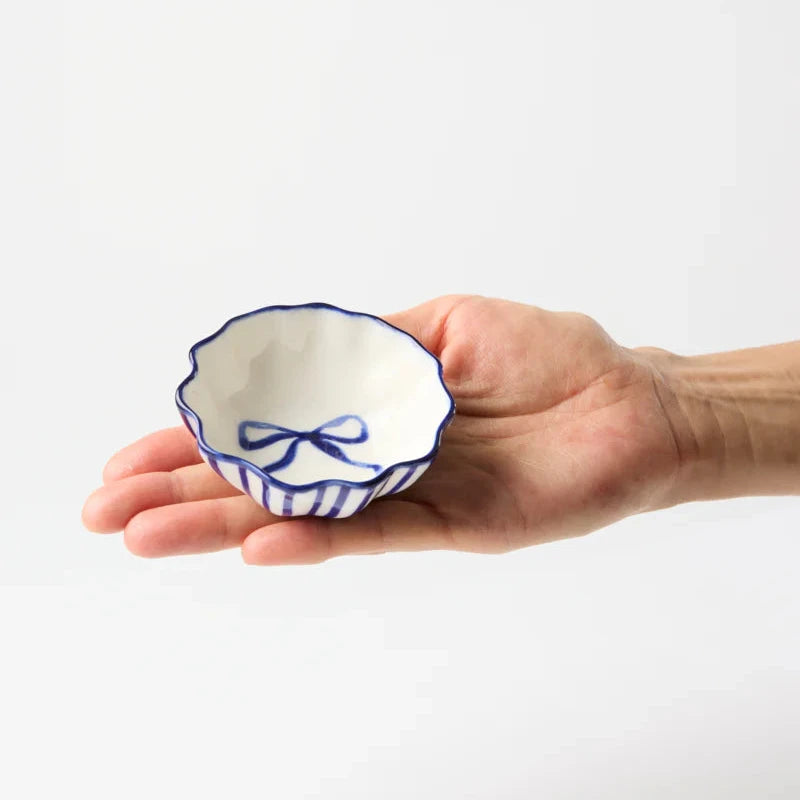 Hand holding a small ceramic bowl with blue decorative elements on a white background