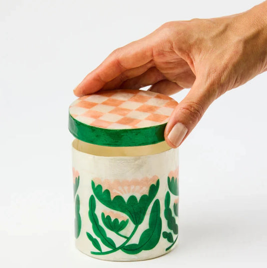 Hand holding a ceramic jar with green lid against a white background