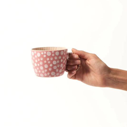Hand holding a pink polka dot mug on a white background