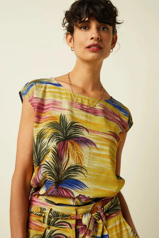 Woman wearing a colourful sleeveless top with a vintage-inspired tropical palm tree print on a plain beige background