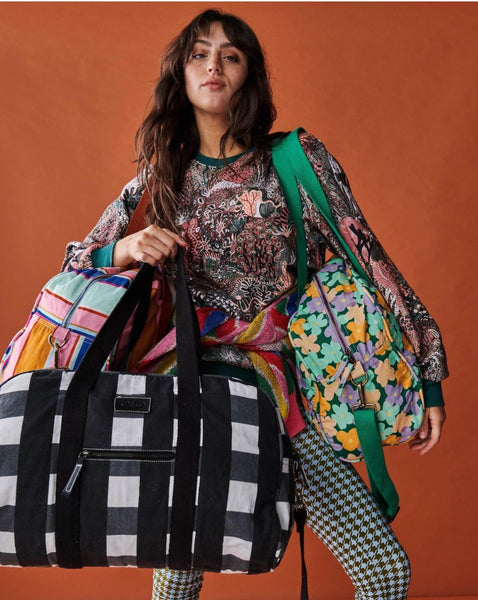 Model is holding Kip & Co Black & White Gingham Duffle Bag in her hand, and carrying 2 other duffle bags of different designs on her shoulders.
