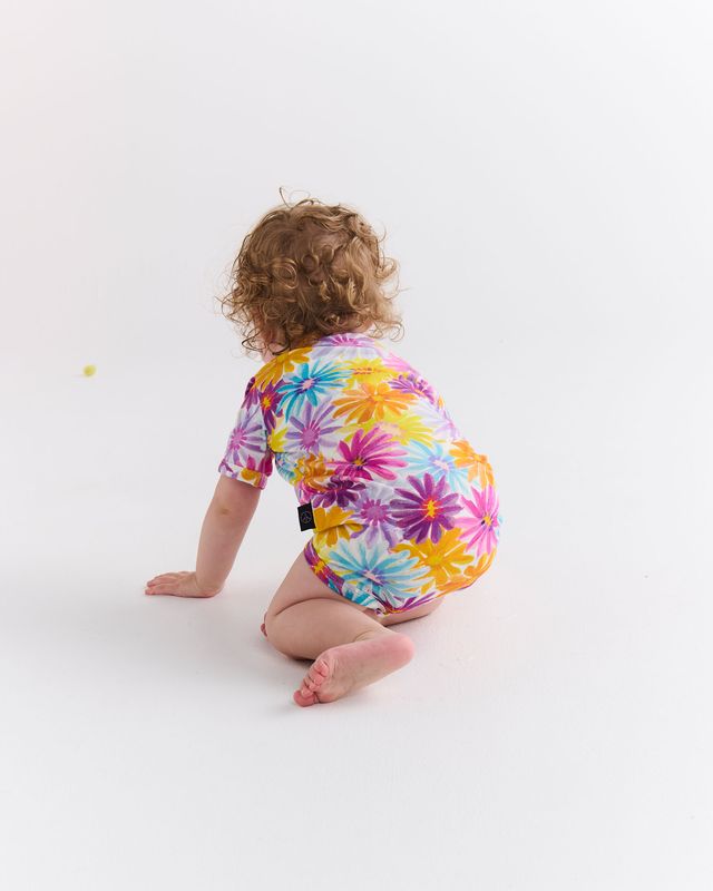 Child wearing a colorful floral onesie on a white background