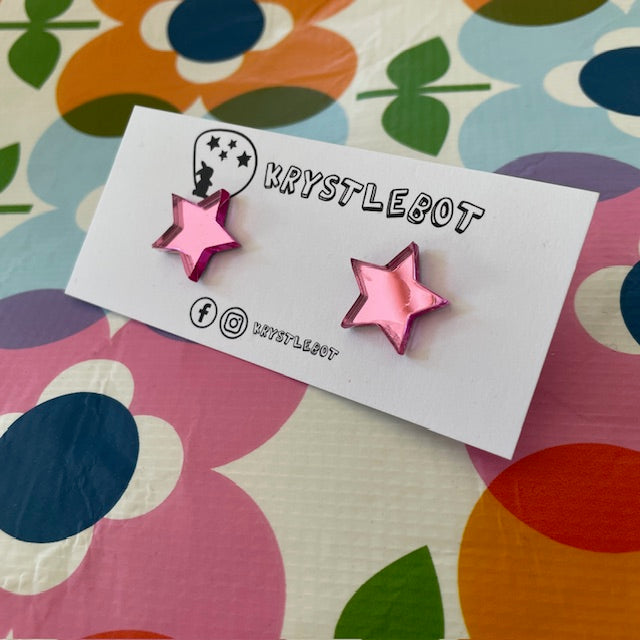 Krystlebot Star Studs - Pink Mirror. Pink star-shaped earrings on a 'KRYSTLEBOT' branded card with a colorful floral background.