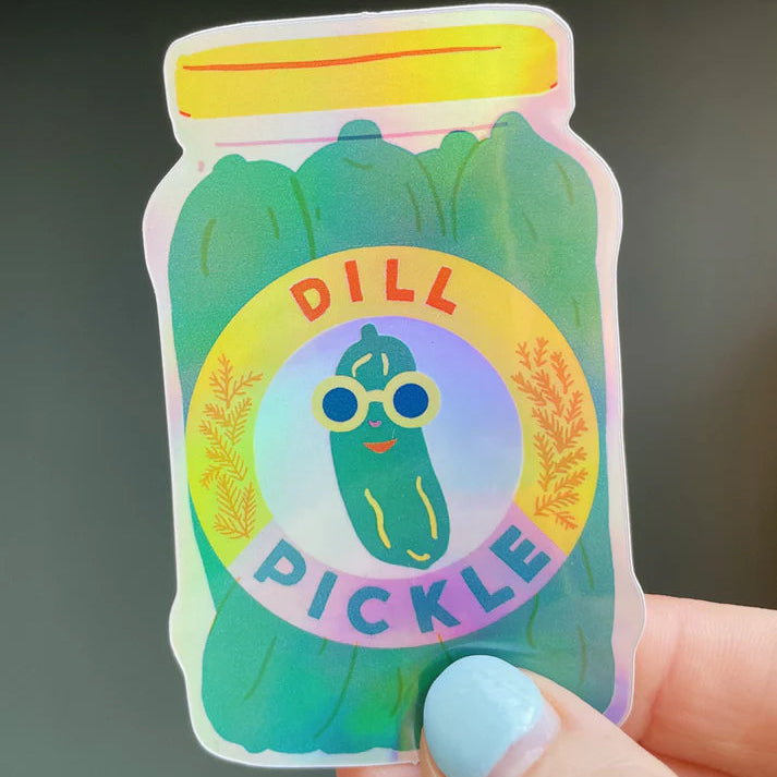 Sticker of a dill pickle jar with a colorful label held by a hand against a dark background