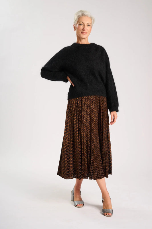 Model wearing a black sweater and pleated brown skirt on a white background