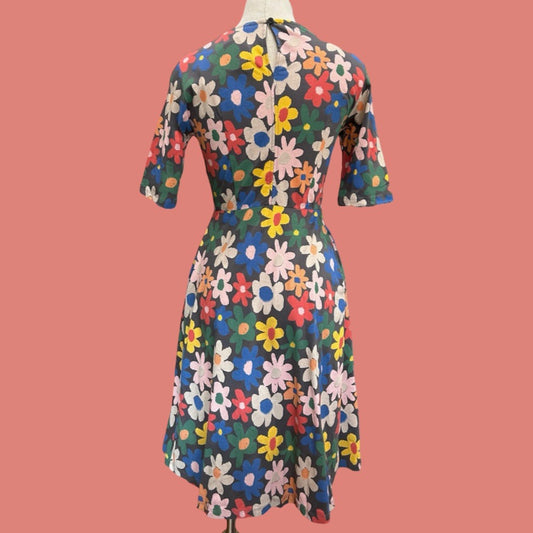 Back view of colourful floral dress on a mannequin against a pink background