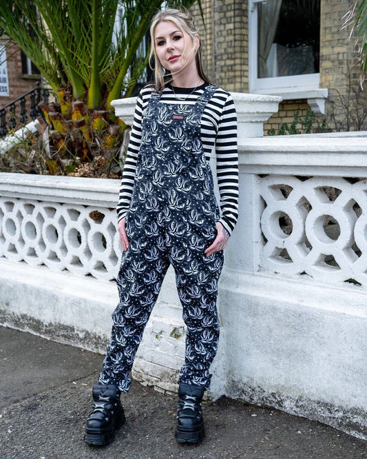 Model is wearing Run and Fly Checkerboard Swallow Twill Dungarees with both thumbs hooked into side pockets.