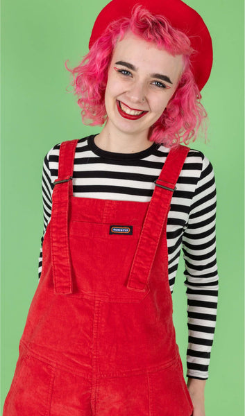 Portrait of model wearing Run & Fly Red Cord Dungarees with a black and white striped long sleeve top underneath.