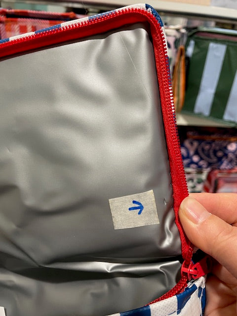 Lid of the Imperfect Mini tote with an arrow sticker pointing to the small cut near the zipper.