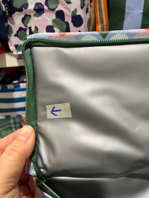 Lid lining of the Imperfect Mini tote with an arrow sticker pointing to a tiny cut approx 1mm near the zipper on the left side.