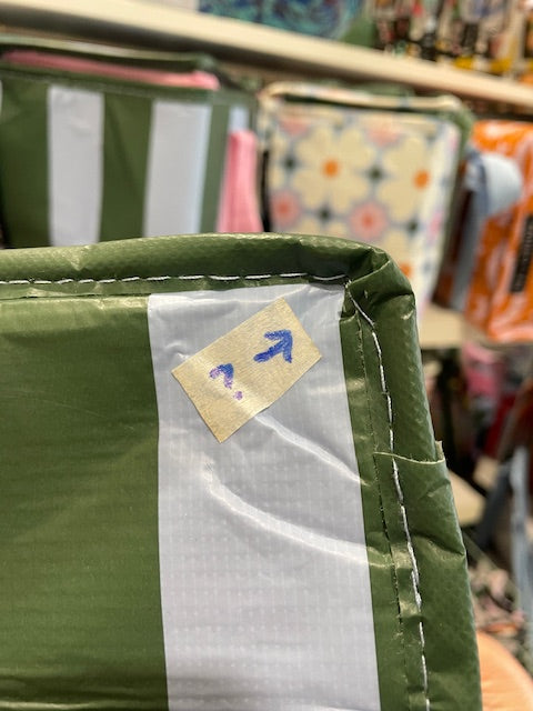 Close up of the right corner of the Base of the tote with arrow sticker pointing to the corner where the trimming has not been sewn well. 