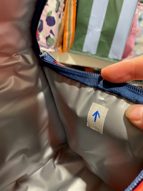 Insulated lining of the Imperfect Mini tote with an arrow sticker pointing to a small cut approx 5mm  near the zipper on the right side.