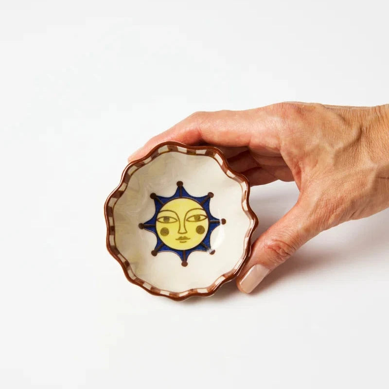 Hand holding a ceramic dish with a sun design on a white background