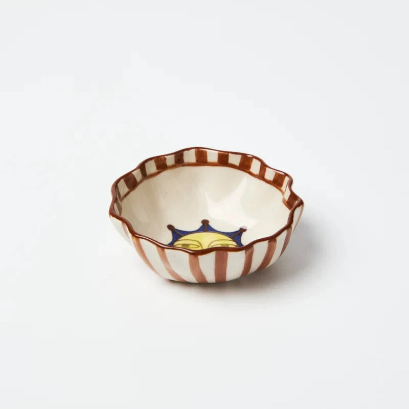 A small ceramic bowl with a scalloped rim, featuring alternating brown and white stripes on the exterior and a small blue and yellow crown motif on the interior, set against a plain white background.