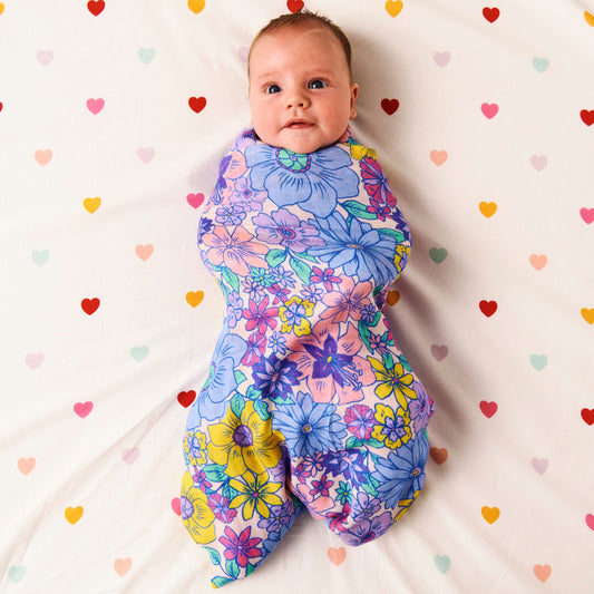 Styled image of Kip & Co Bunch of Fun Bamboo Baby Swaddle wrapped around a baby on a bed with hearts on the bedsheet.