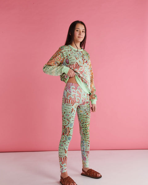 Model is standing side on from the camera and has lifted up one of the sides of the jumper. She is wearing Kip&Co X Ernabella Arts Ngayaku Ngura Adult Organic Cotton Sweater. Featung artwork by Ernabella Arts artist Rupert Jack.