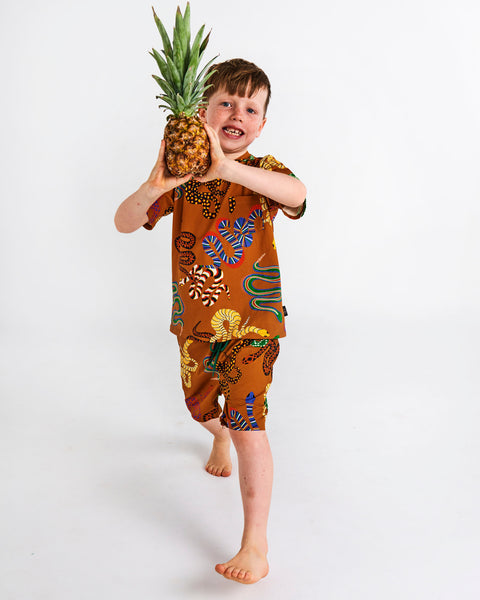 Kip & Co Snake Pit Kid's Tee worn by a young model with matching shorts holding a pineapple