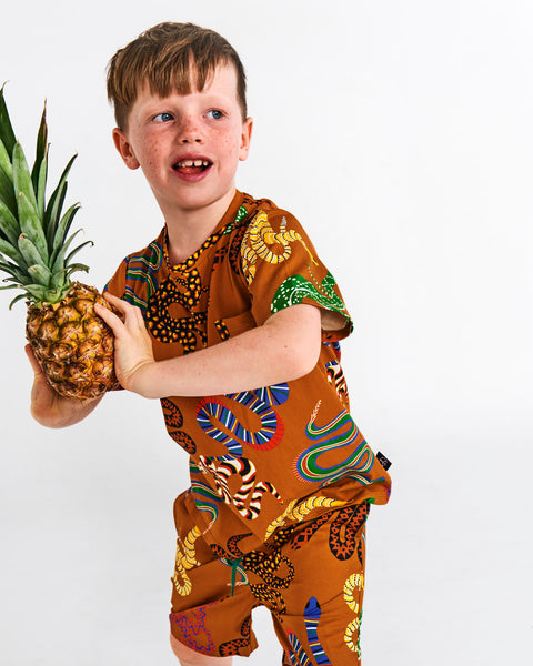 Kip & Co Snake Pit Kid's Tee worn by a young model and matching shorts holding a pineapple like he is about to throw it to someone