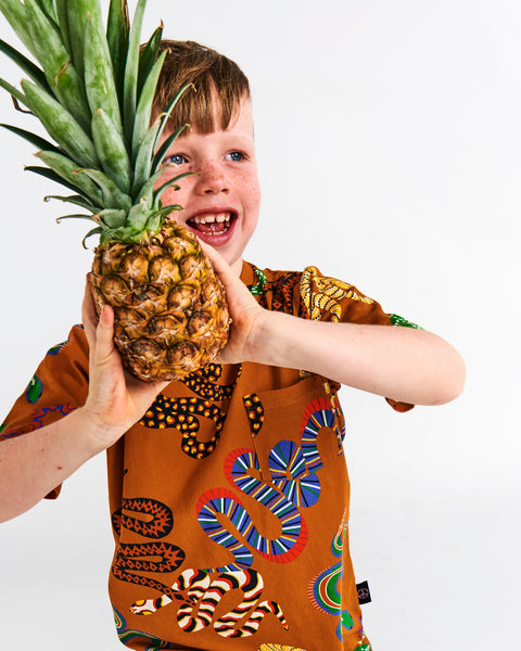 Kip & Co Snake Pit Kid's Tee worn by a young model holding a pineapple with both hands.