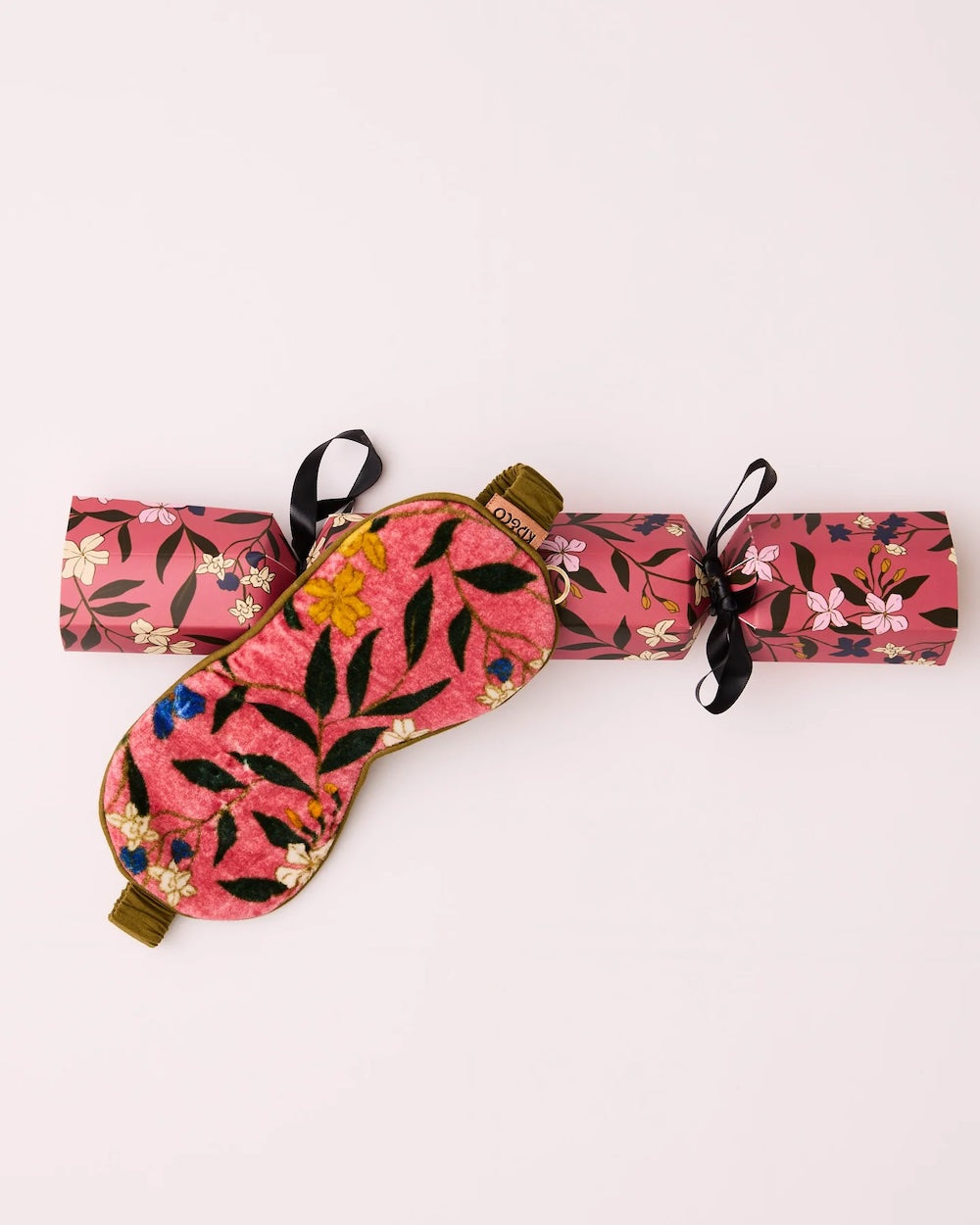 A Kip&Co Canopy Rose Velvet Eye Mask laid over its matching packing that looks like a Christmas bon-bon.