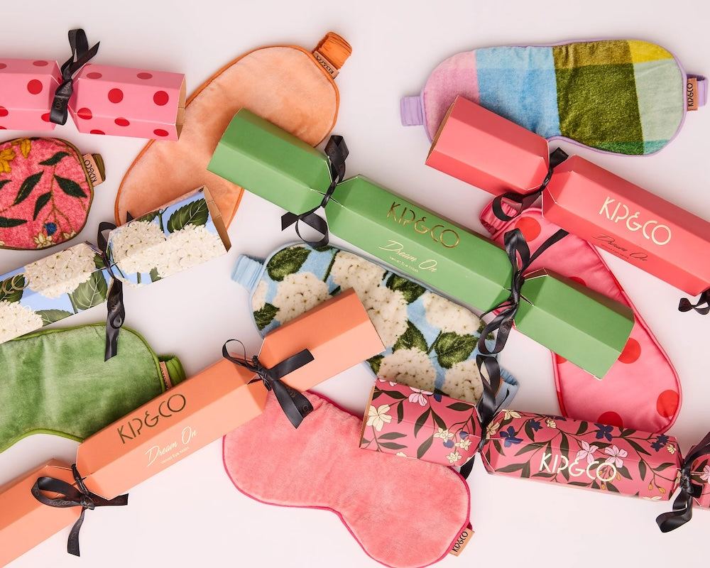 A styled flatlay of many colourful Kip&Co velvet sleep masks with their matching Christmas bon-bon-shaped gift boxes.