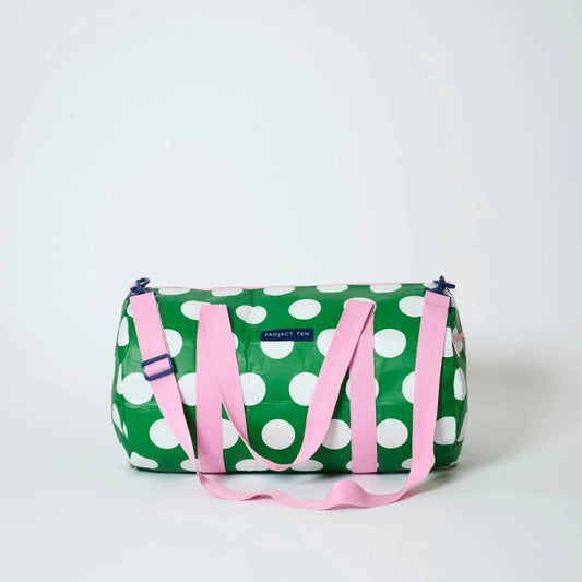 Green duffel bag with white polka dots and pink straps on a light gray background