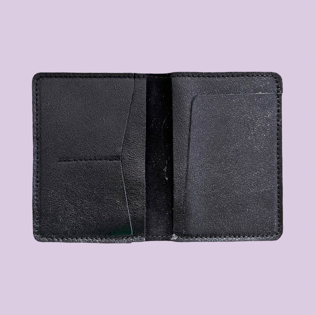 Black leather passport holder open on a light purple background
