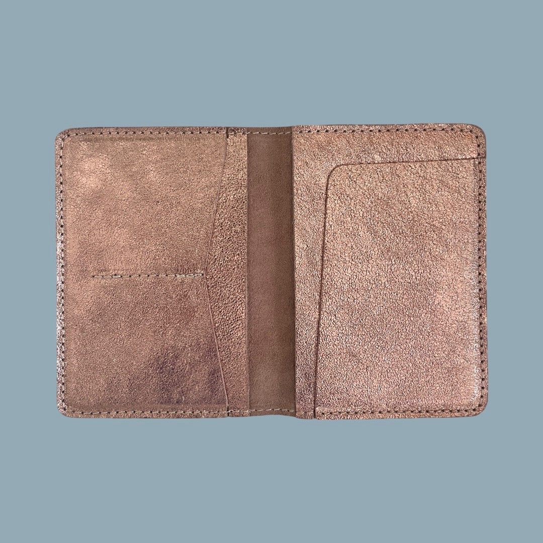 A pale rose pink leather passport holder opened, displayed flat against a solid slate blue background.