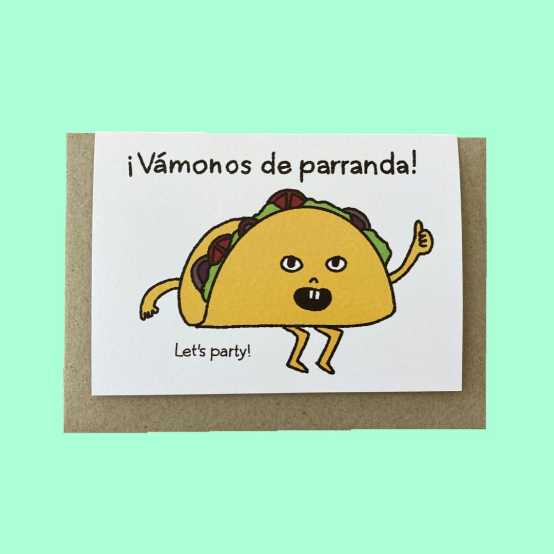 A white greeting card with a brown kraft envelope, featuring a cartoon taco character and the Spanish text '¡Vámonos de parranda!' with 'Let's party!' below, set against a solid mint green background.
