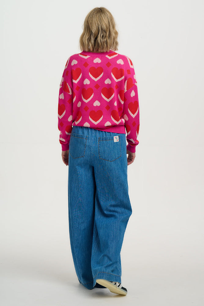 Person wearing a pink sweater with heart patterns and blue jeans on a white background