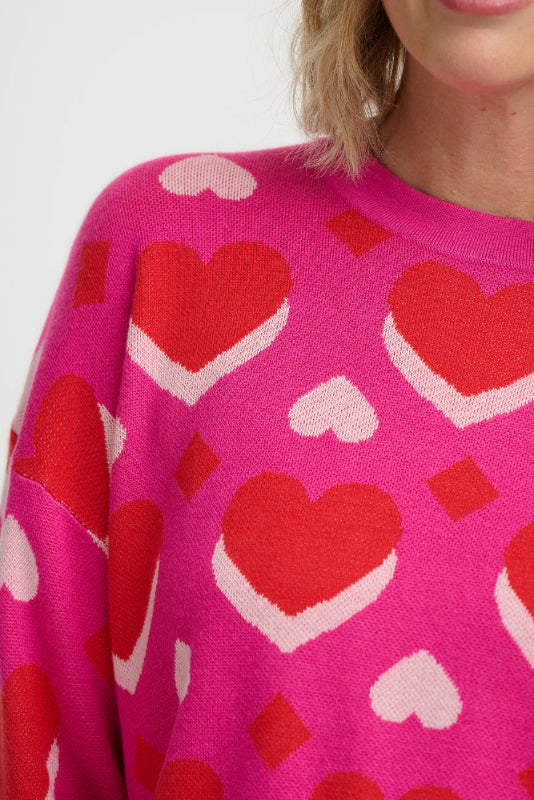 Person wearing a pink sweater with red heart patterns on a white background