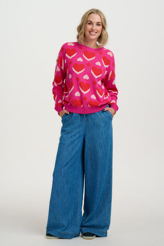 Woman wearing a pink sweater with heart patterns and blue jeans on a white background