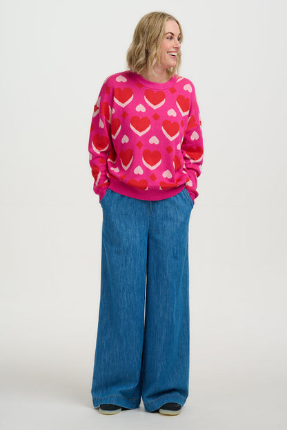 Person wearing a pink sweater with red heart patterns and blue jeans on a white background