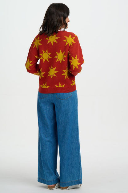Back view of Person wearing a red sweater with yellow sun patterns and blue jeans on a white background